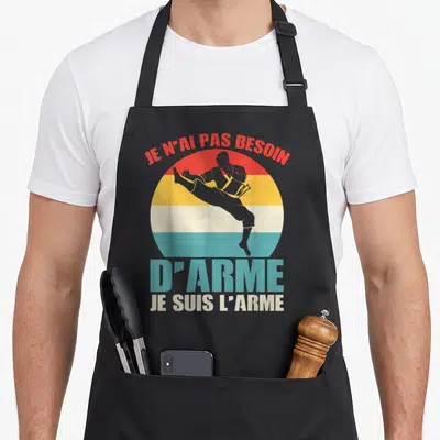 Tablier de cuisine noir avec une silhouette de combattant et le texte Je suis l'arme en style vintage.