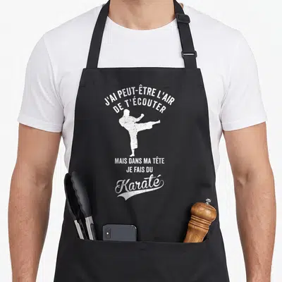 Tablier de cuisine noir avec une silhouette blanche effectuant un coup de pied et le texte J'ai peut-être l'air de t'écouter mais dans ma tête je fais du Karaté.