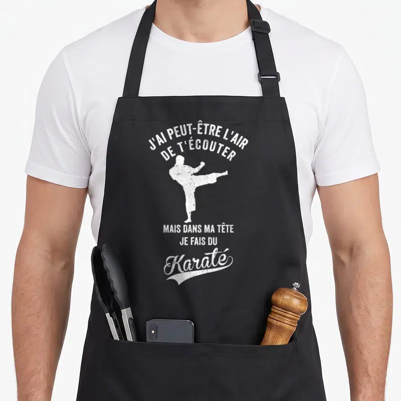 Tablier de cuisine noir avec une silhouette blanche effectuant un coup de pied et le texte J'ai peut-être l'air de t'écouter mais dans ma tête je fais du Karaté.