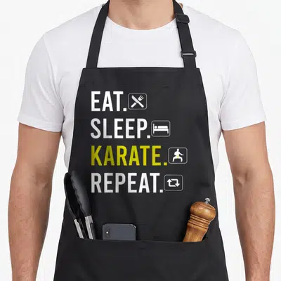 Tablier de cuisine noir avec l'inscription Eat Sleep Karate Repeat en blanc et jaune accompagnée d'icônes minimalistes.