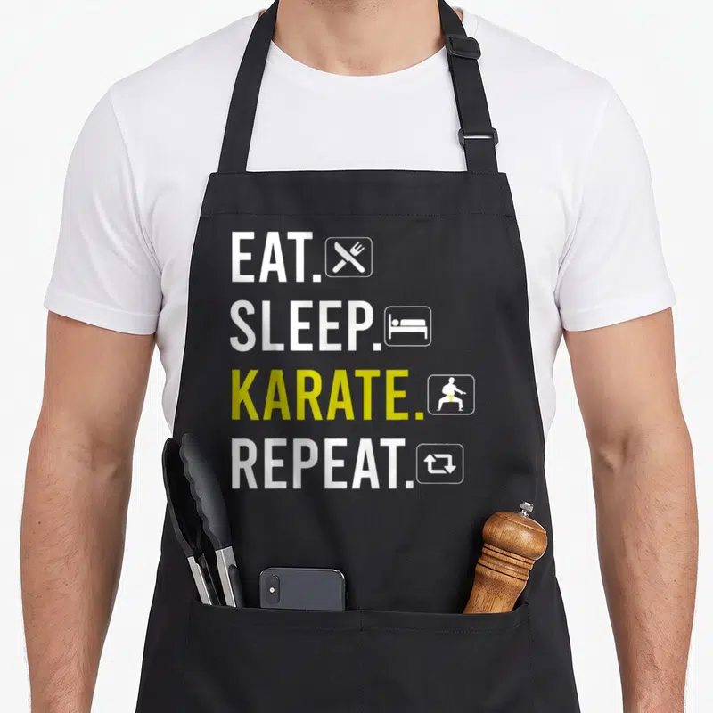 Tablier de cuisine noir avec l'inscription Eat Sleep Karate Repeat en blanc et jaune accompagnée d'icônes minimalistes.