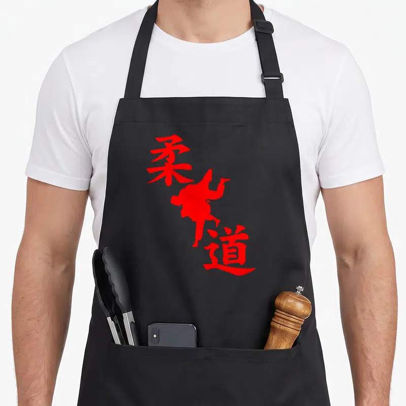 Tablier de cuisine noir avec silhouette rouge d'un judoka effectuant un mouvement et des caractères kanji verticaux.