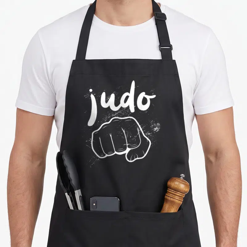 Tablier de cuisine noir avec le mot judo et un poing ferm dessiné en blanc au centre