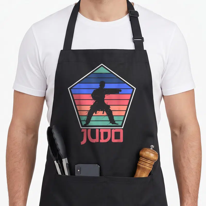 Tablier de cuisine noir avec logo pentagonale Judo retro et silhouette de pratiquant en position de combat.