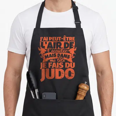 Tablier de cuisine noir avec typographie orange et silhouettes de judokas en position de combat.