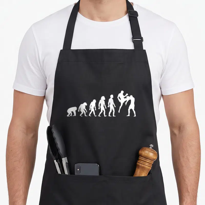 Tablier de cuisine noir avec une illustration blanche représentant l'évolution humaine se terminant par des silhouettes de kickboxeurs en pleine action.