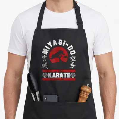 Tablier de cuisine noir avec logo Miyagi-Do, soleil rouge, arbre et texte Karate Reseda CA en blanc et rouge.