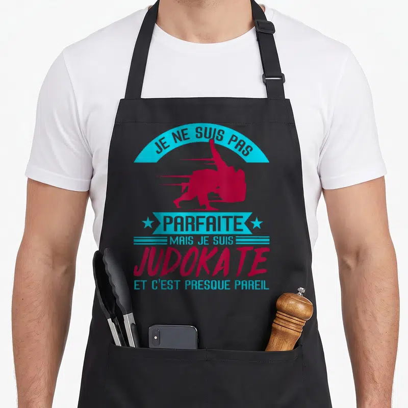 Tablier de cuisine noir avec silhouette judokate rose et texte bleu cyan sur fond uni.