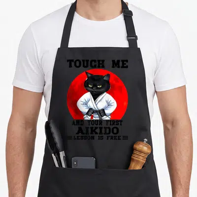 Tablier de cuisine noir avec un chat noir en kimono blanc devant un cercle rouge et du texte humoristique en anglais.