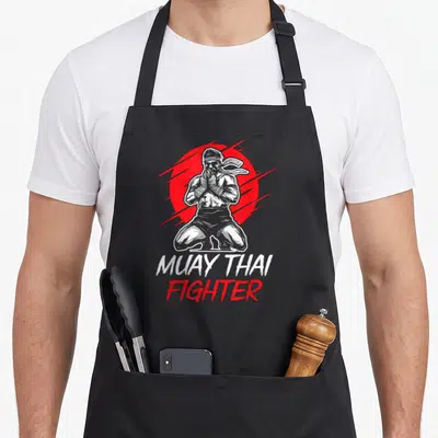 Tablier de cuisine noir avec illustration d'un combattant de Muay Thai et le texte Muay Thai Fighter sur fond rouge.