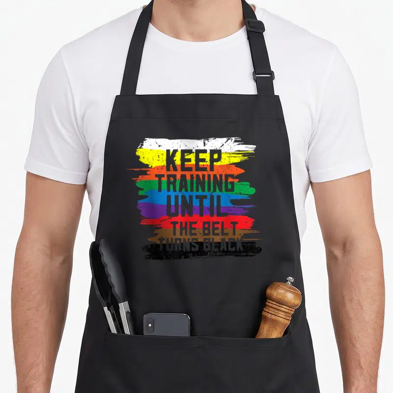 Tablier de cuisine noir avec inscription Keep Training Until The Belt Turns Black sur bandes colorées style brusho.