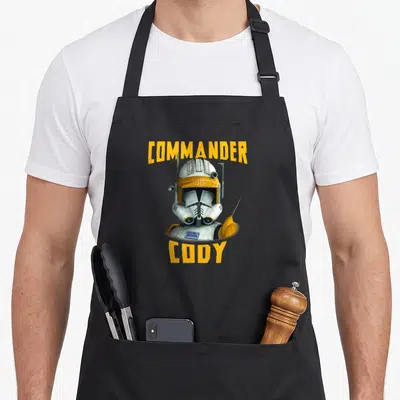 Tablier de cuisine noir avec illustration du commandant Cody et texte jaune.
