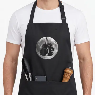 Tablier de cuisine noir avec gants de boxe suspendus devant une lune détaillée en gris et blanc.