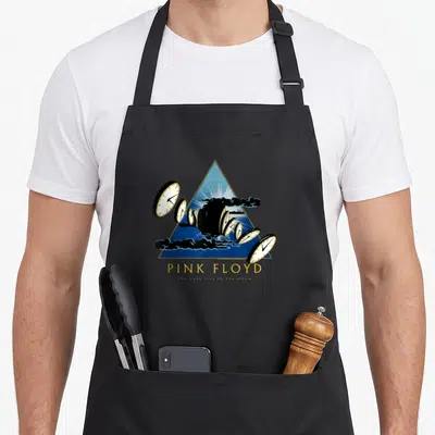 Tablier de cuisine noir avec motif triangle bleu, horloges fondantes et texte Pink Floyd The Dark Side of the Moon en lettres dorées.