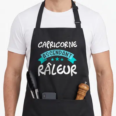 Tablier de cuisine noir avec linscription Capricorne ascendant râleur en blanc sur bandeau bleu turquoise et trois étoiles.