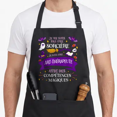 Tablier de cuisine noir avec inscription humoristique sur art-thérapie et motifs d'Halloween comme des chauves-souris et un balai.