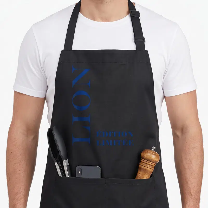 Tablier de cuisine noir avec inscription verticale LION et « ÉDITION LIMITÉE » en bleu marine.