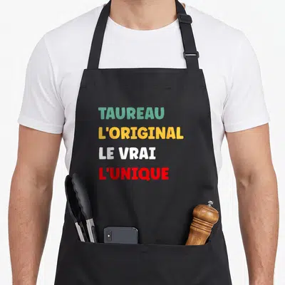 Tablier de cuisine noir avec inscription TAUREAU L'ORIGINAL LE VRAI L'UNIQUE en lettres colorées.