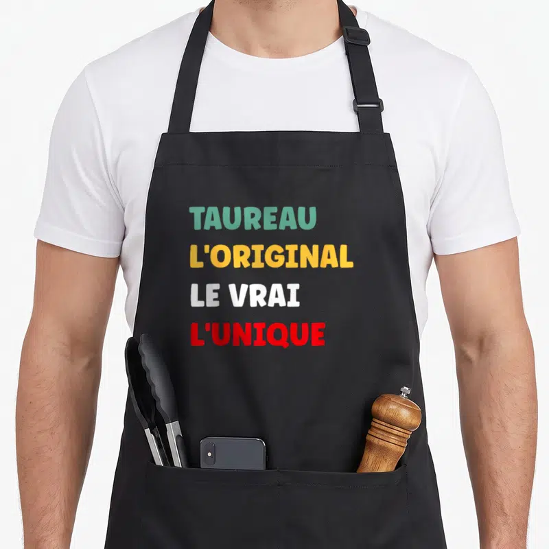 Tablier de cuisine noir avec inscription TAUREAU L'ORIGINAL LE VRAI L'UNIQUE en lettres colorées.