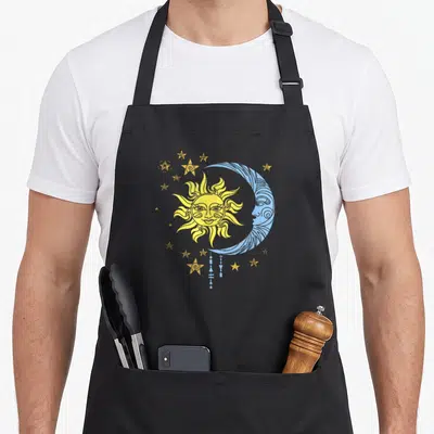Tablier de cuisine noir avec illustration de soleil jaune, lune bleue et étoiles dorées style ésotérique.