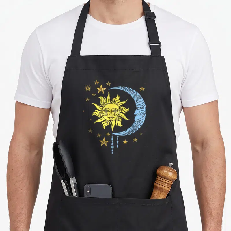 Tablier de cuisine noir avec illustration de soleil jaune, lune bleue et étoiles dorées style ésotérique.