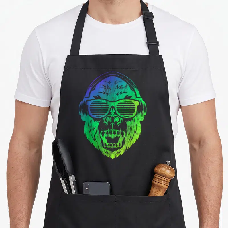 Tablier de cuisine noir avec illustration d'un singe DJ aux couleurs dégradées vert et bleu portant des écouteurs et des lunettes à rayures.