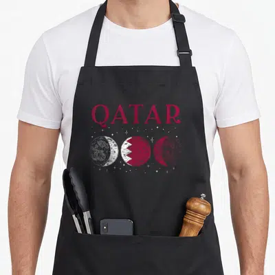 Tablier de cuisine noir avec l'inscription QATAR et trois représentations lunaires stylisées en blanc et bordeaux.
