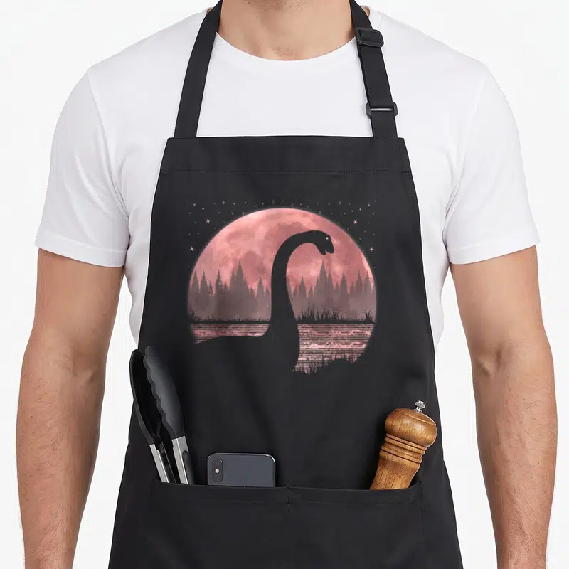 Tablier de cuisine noir avec silhouette du monstre du Loch Ness devant une pleine lune rose et des étoiles.