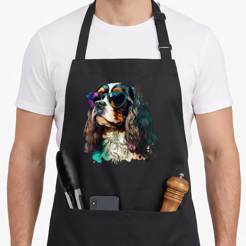 Tablier de cuisine noir avec illustration d'un chien Cavalier King Charles Spaniel en lunettes de soleil colorées et style artistique.