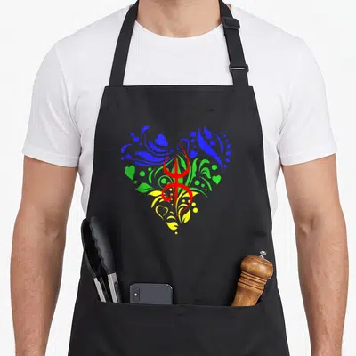 Tablier de cuisine noir avec un grand cœur multicolore contenant le symbole Tifinagh rouge au centre.