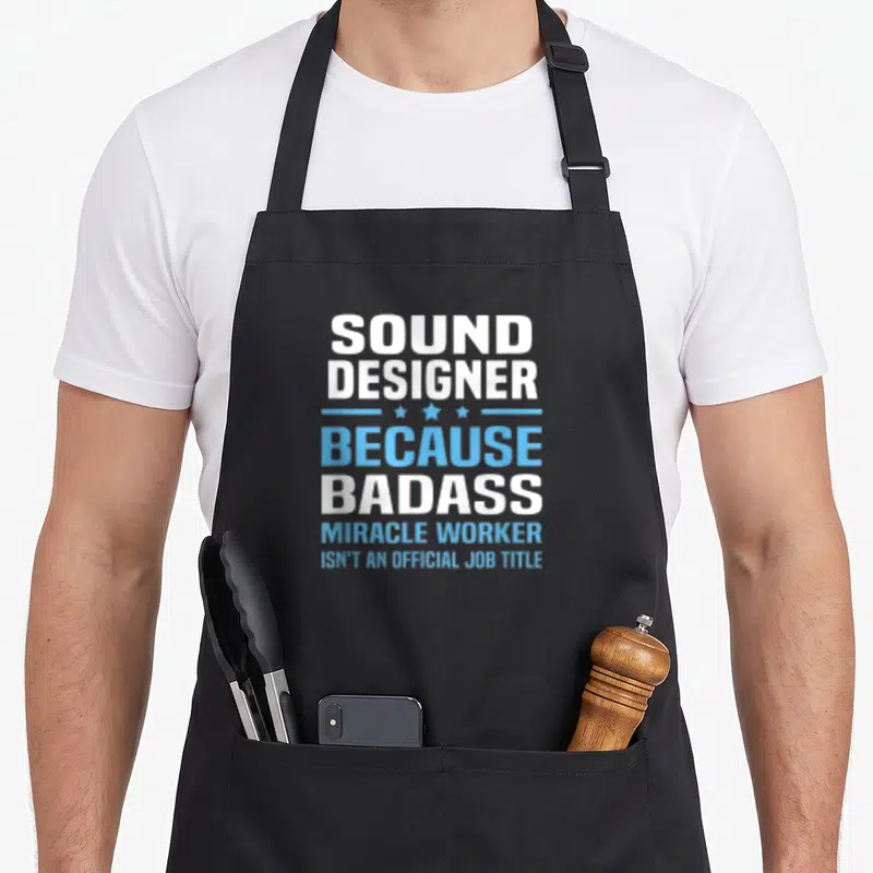 Tablier de cuisine noir avec l'inscription Sound Designer Because Badass Miracle Worker en blanc et bleu.