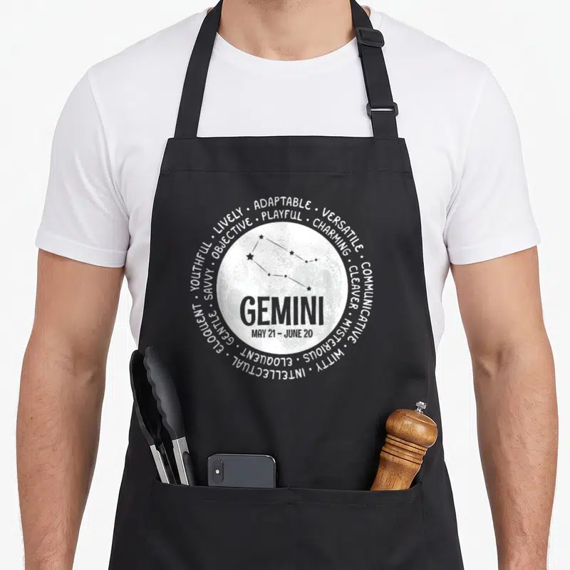 Tablier de cuisine noir avec motif circulaire blanc représentant le signe Gemini et ses traits de caractère.