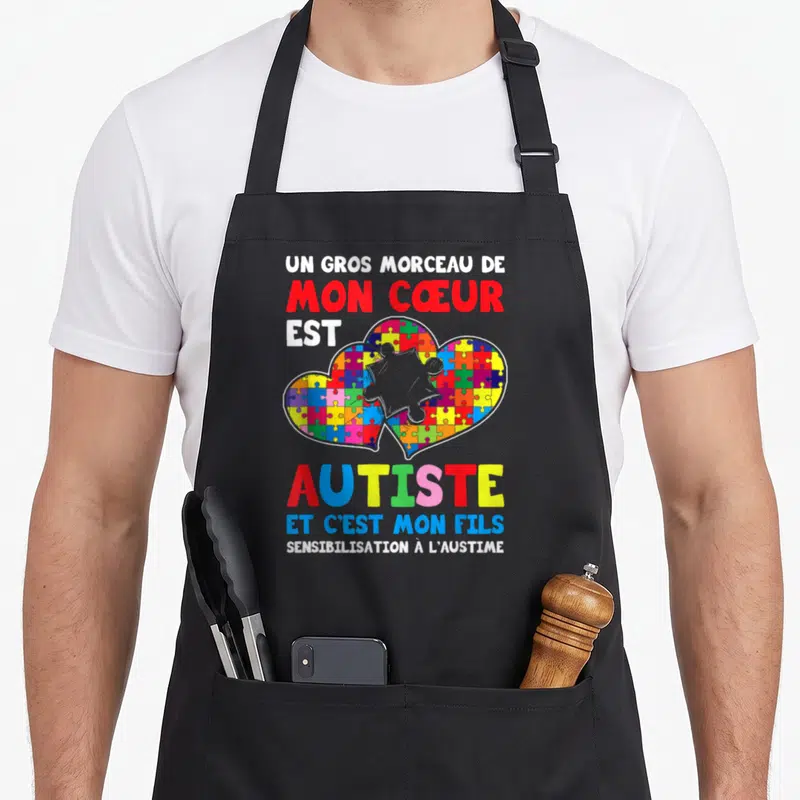 Tablier de cuisine noir avec un cœur de puzzle multicolore et le texte Mon cœur est autiste et c'est mon fils.