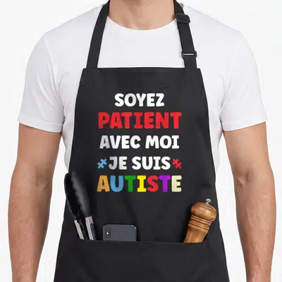 Tablier de cuisine noir avec inscription Soyez patient avec moi je suis autiste en lettres blanches, rouges et multicolores.