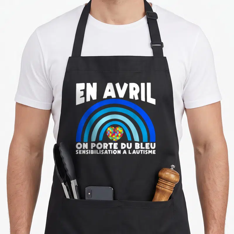 Tablier de cuisine noir avec arc-en-ciel bleu et cœur en puzzle coloré au centre.