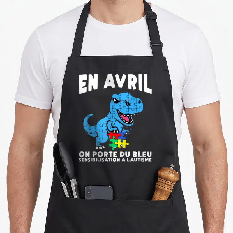 Tablier de cuisine noir avec un dinosaure bleu en puzzle tenant des pièces colorées et du texte blanc.
