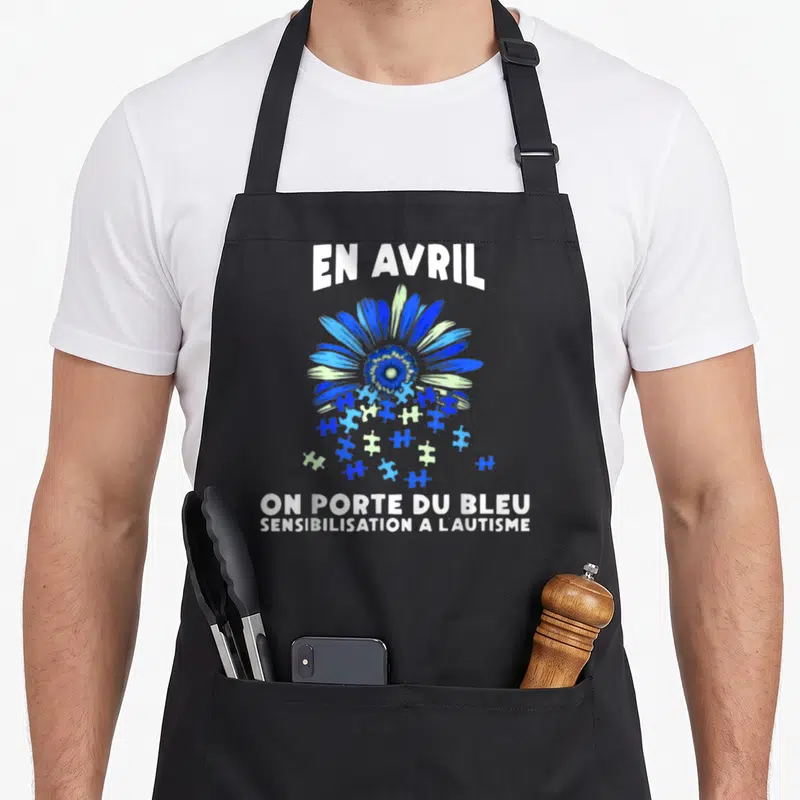 Tablier de cuisine noir avec une fleur stylisée aux nuances de bleu et des pièces de puzzle évoquant la sensibilisation à l'autisme.