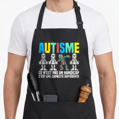 Tablier de cuisine noir avec quatre squelettes dont un multicolore et un message sur l'autisme imprimé en blanc.