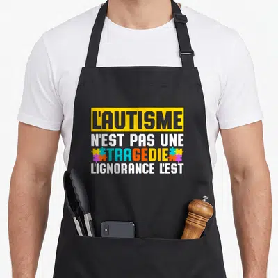 Tablier de cuisine noir avec un message typographique multicolore sur la sensibilisation à l'autisme et des motifs de puzzle.