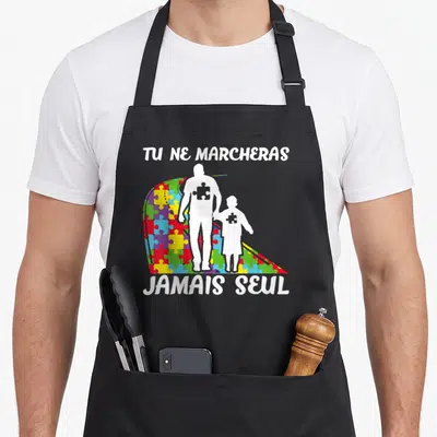 Tablier de cuisine noir avec silhouettes blanches tenant la main devant un arc en ciel de pièces de puzzle multicolores et texte blanc.