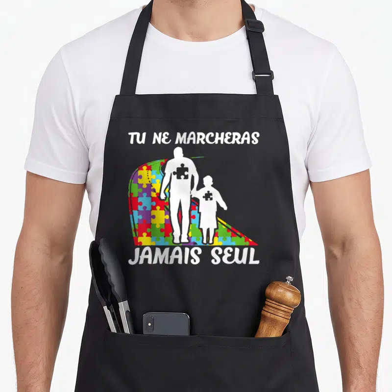 Tablier de cuisine noir avec silhouettes blanches tenant la main devant un arc en ciel de pièces de puzzle multicolores et texte blanc.