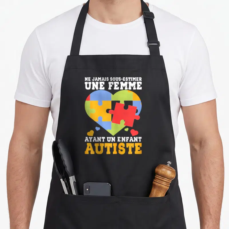 Tablier de cuisine noir avec un cœur en puzzle multicolore et un texte blanc sur fond uni.