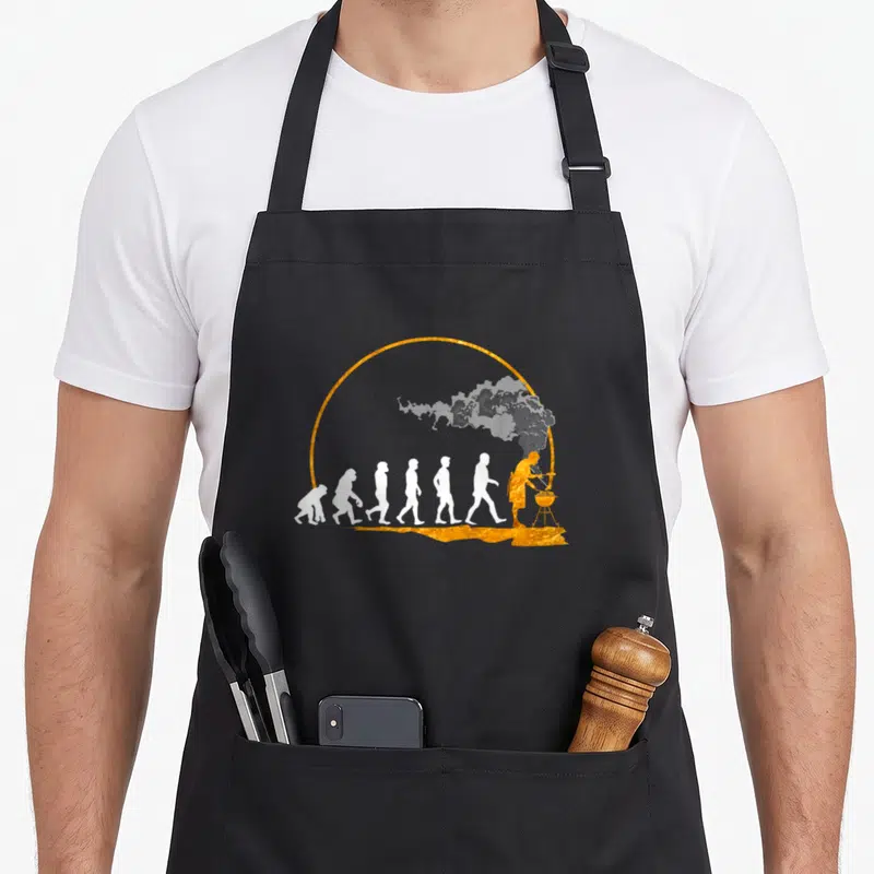 Tablier de cuisine noir avec illustration dorée et blanche représentant l'évolution humaine vers le grillage.