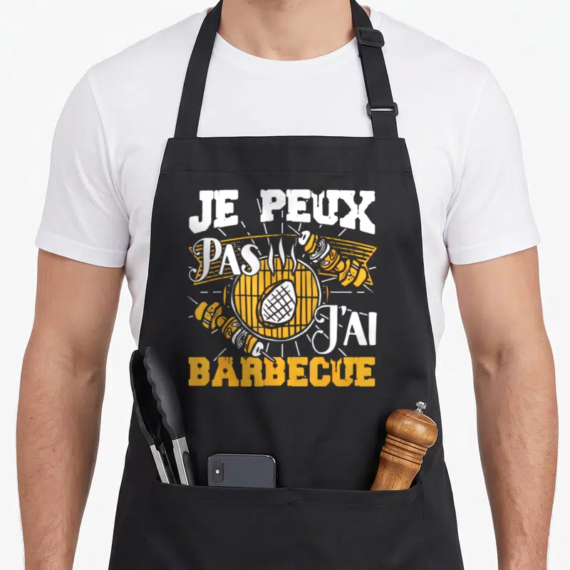 Tablier de cuisine noir avec inscription Je peux pas j'ai barbecue et illustration de grill orange et blanc.