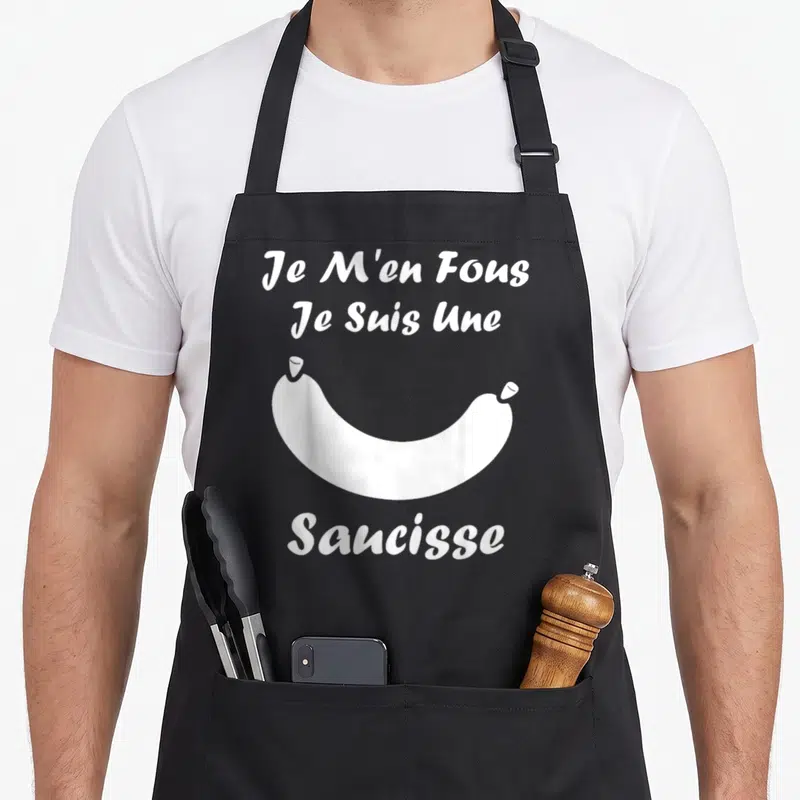 Tablier de cuisine noir avec une illustration de saucisse blanche et le texte Je M'en Fous Je Suis Une Saucisse.