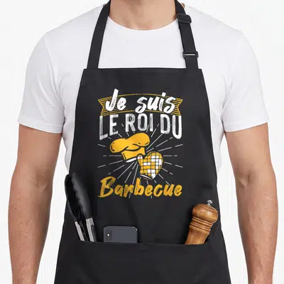 Tablier de cuisine noir avec inscription Je suis le roi du Barbecue et illustration de toque jaune.