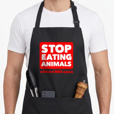 Tablier de cuisine noir avec un logo carré rouge affichant le texte Stop Eating Animals without BBQ sauce en blanc et rouge.
