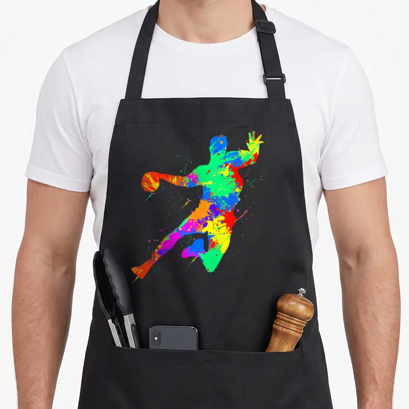 Tablier de cuisine noir avec une silhouette de joueur de handball aux couleurs vives et aux effets d'éclaboussures artistiques.
