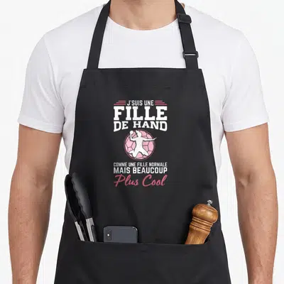 Tablier de cuisine noir avec inscription Fille de Hand et silhouette blanche sur balle rose.