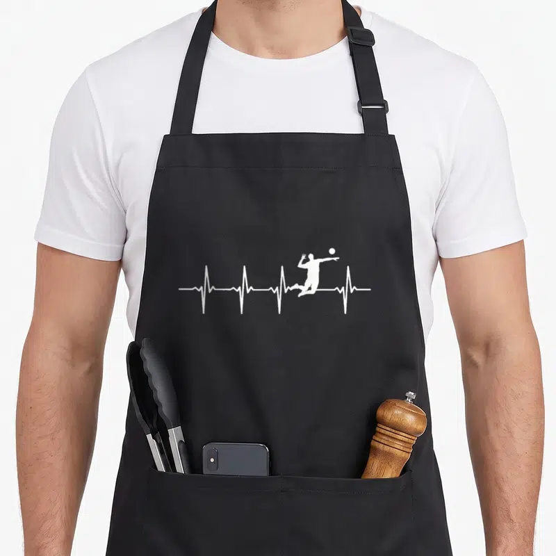 Tablier de cuisine noir avec un graphique blanc représentant une ligne d'électrocardiogramme et la silhouette d'un joueur de volley en saut.